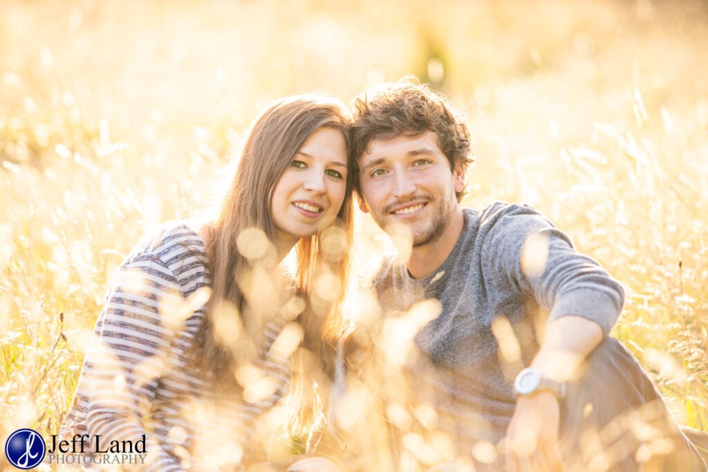 A man and woman are sitting in a field of tall grass during their pre-wedding shoot in Warwick.